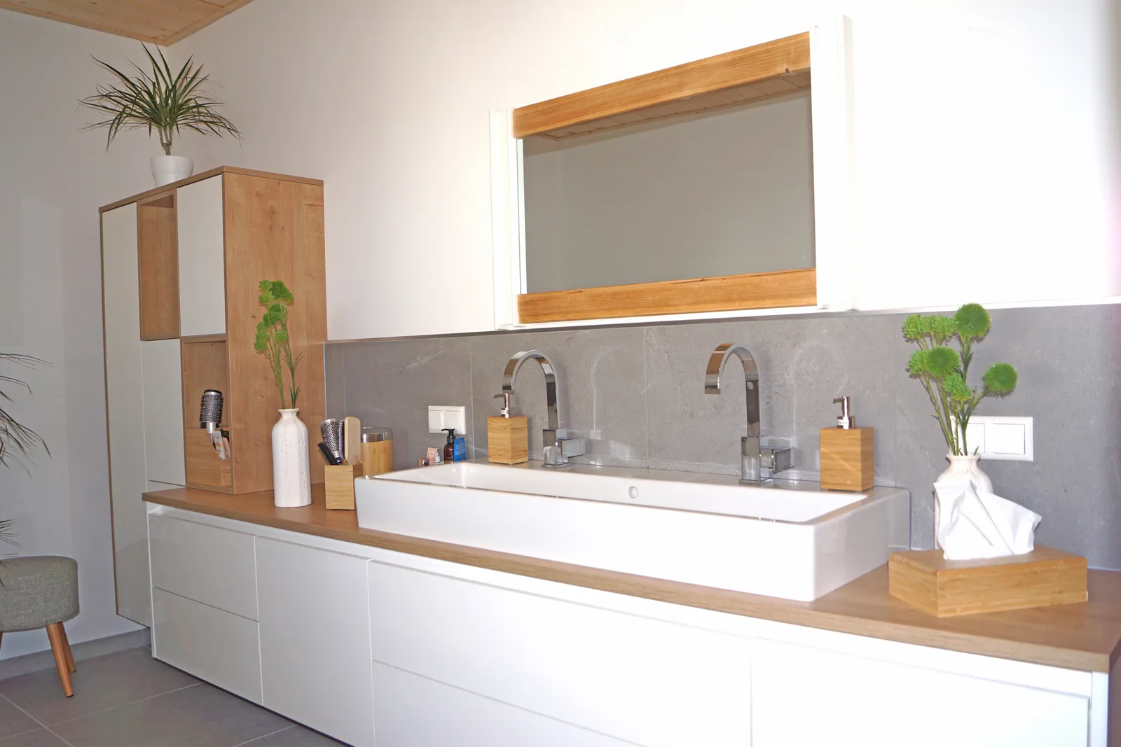 Helles Bad mit langem weißem Waschtisch, Holzplatte, zwei Armaturen, Spiegel mit Holzrahmen und Hochschrank