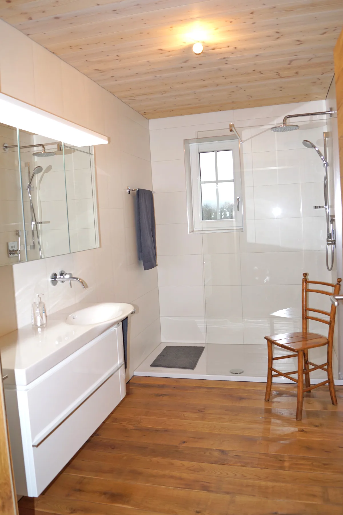 Bad mit Holzdecke und Holzboden, bodengleiche Dusche mit Glaswand und weißer Waschtisch