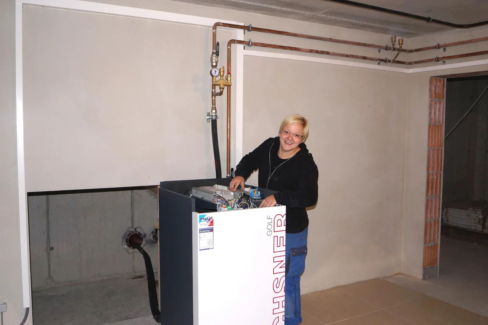 Monteurin schließt eine Ochsner-Wärmepumpe in einem Technikraum im Rohbau an, an der Wand Kupferleitungen