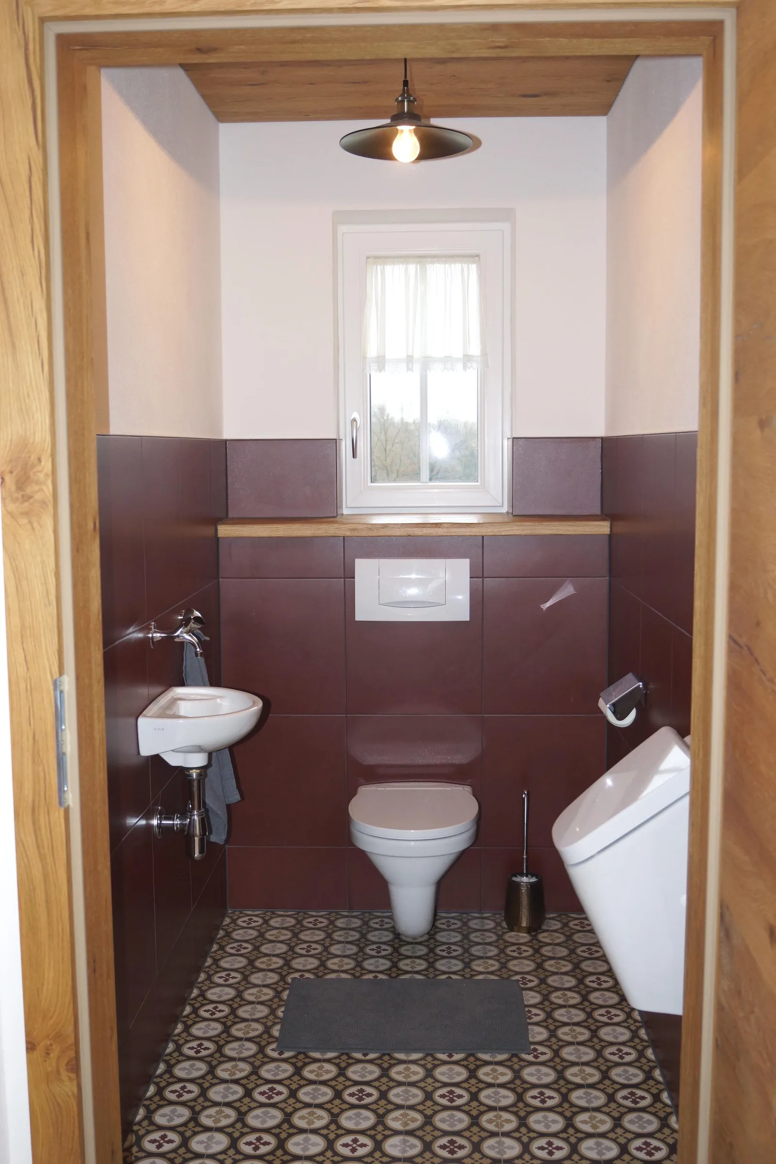WC mit bordeauxroten Wandfliesen, gemustertem Zementfliesenboden und Holzzarge